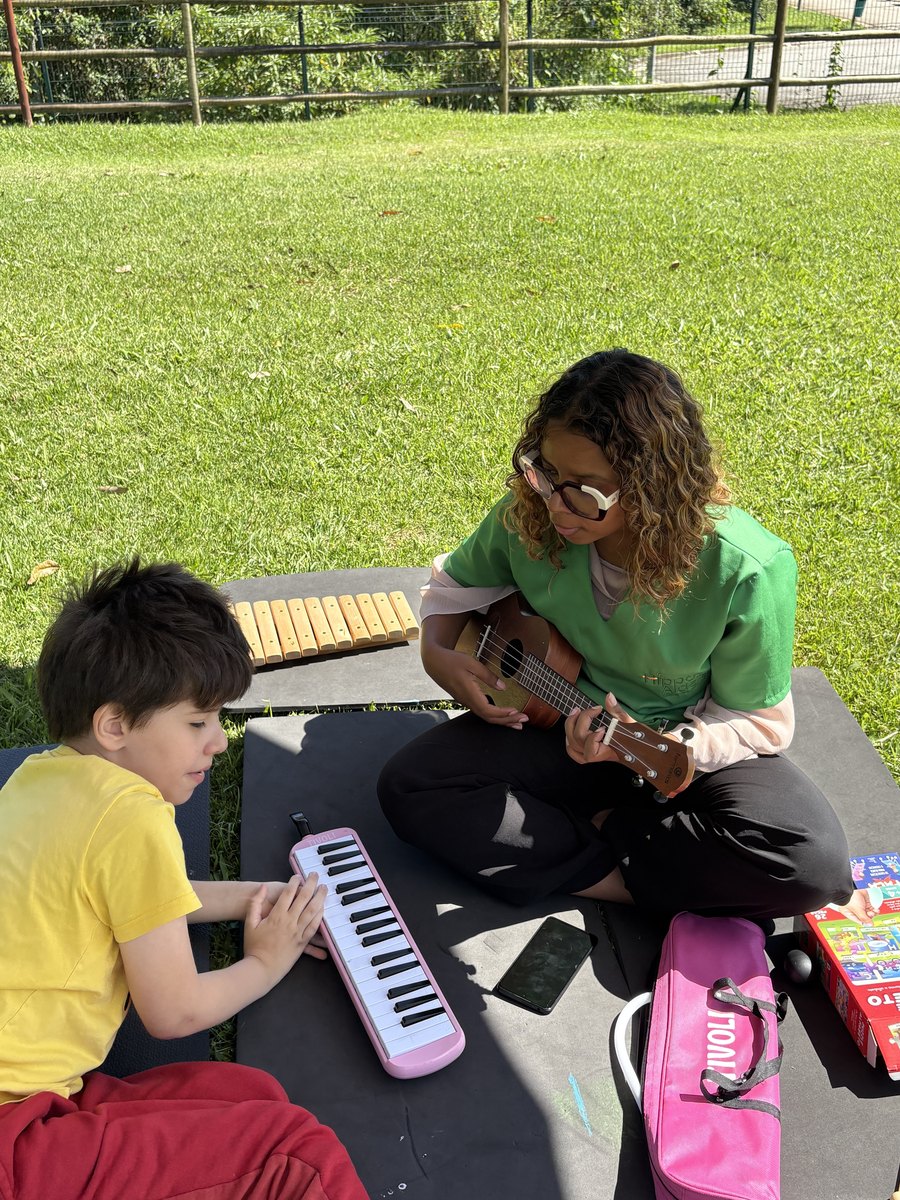 Sessão de musicoterapia ao ar livre na Hippus Aldeia: criança com escaleta e musicoterapeuta com ukulele