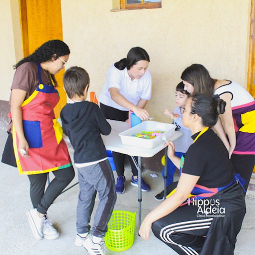 Equipe interdisciplinar da Hippus Aldeia em atividade lúdica com crianças ao redor de uma mesa